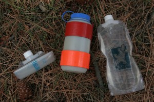 The Nalgene bottle, center, has a piece of parachute cord secured with duct tape. This would allow the bottle to be tied to a rope and lowered into a pool. The nalgene is flanked by two collapsible soft bottles. 